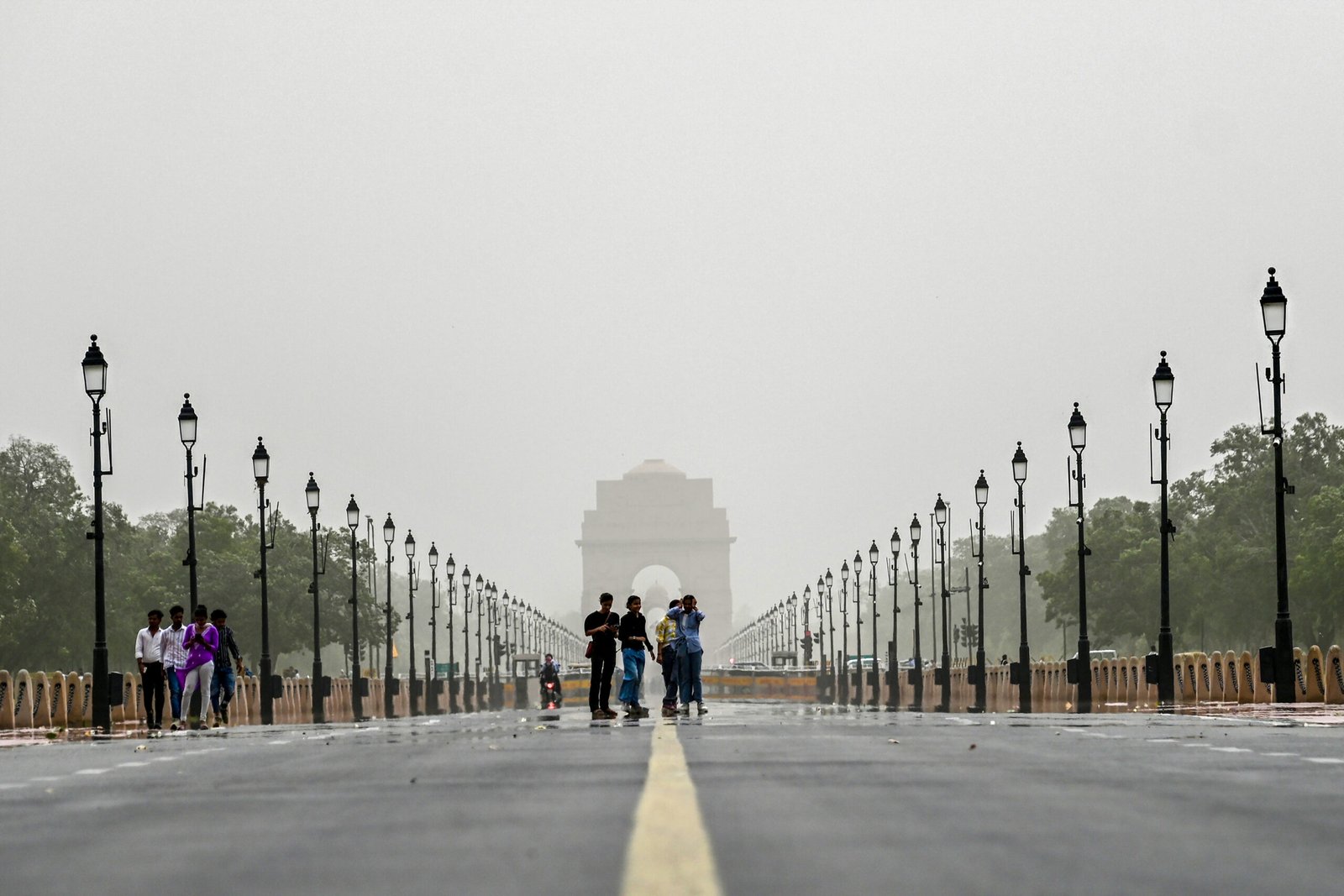 Dark monsoon clouds hang over Delhi as people walk with umbrellas along a rain-soaked street during a spell of rainfall.