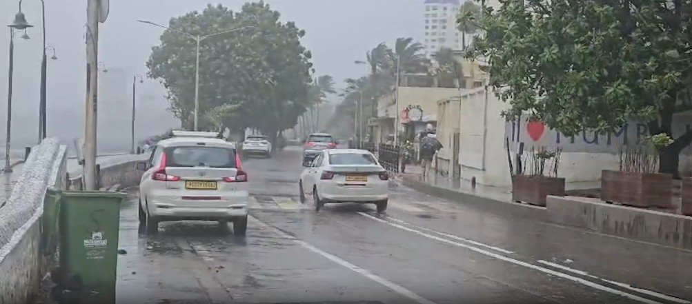 Heavy rain inundates a road in Mumbai as commuters wade through waterlogged streets while vehicles move slowly amid severe monsoon conditions.