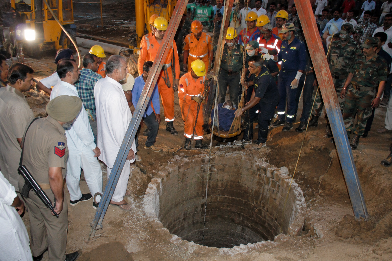 Rescue personnel and emergency responders gather around a deep borewell during a nighttime rescue operation in Haryana's Ambala district after a young child fell inside, with heavy machinery and police deployed at the site.