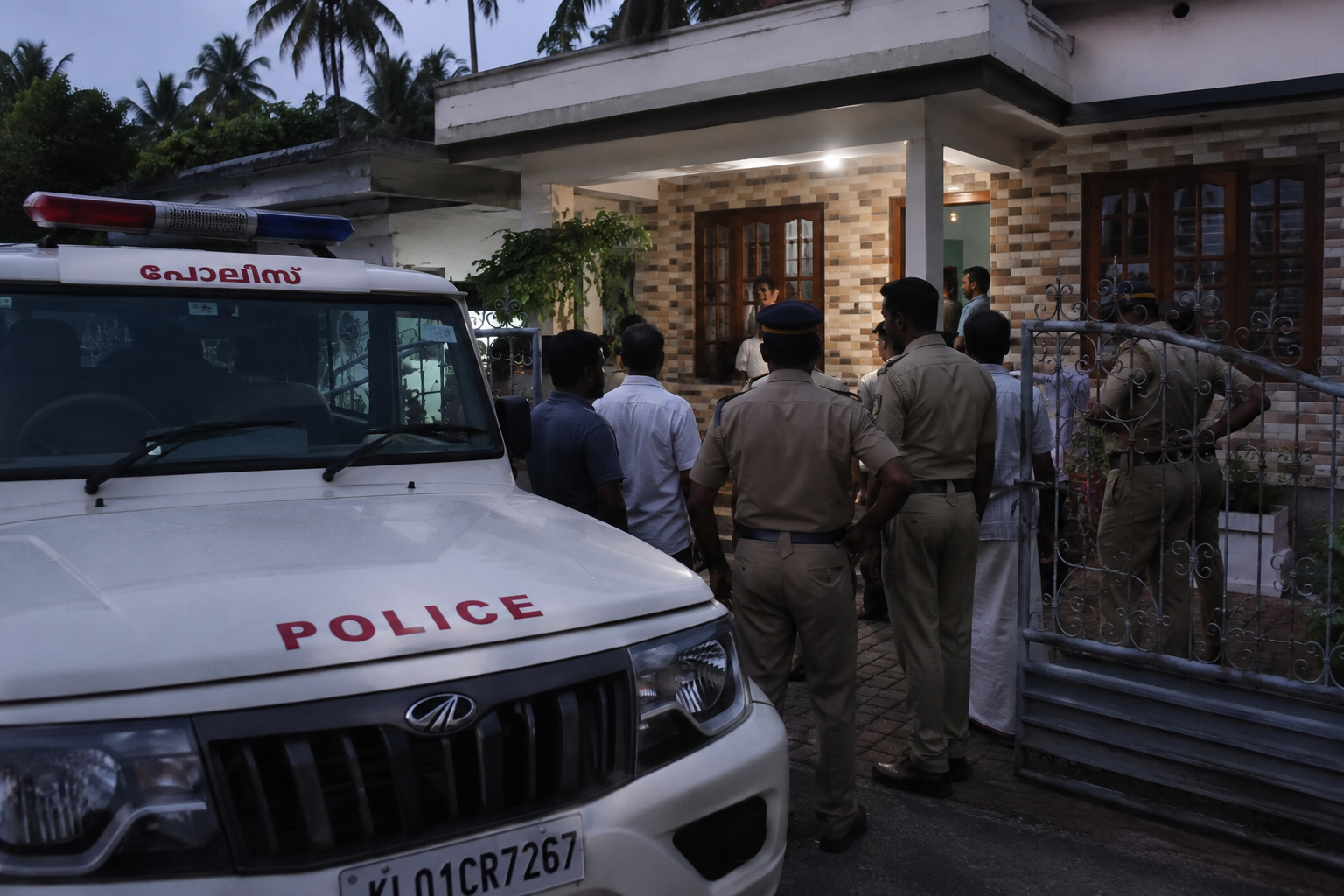 Police officers and local residents gather outside a house during an evening investigation following the reported death of a 27-year-old woman near Vizhinjam, Kerala.