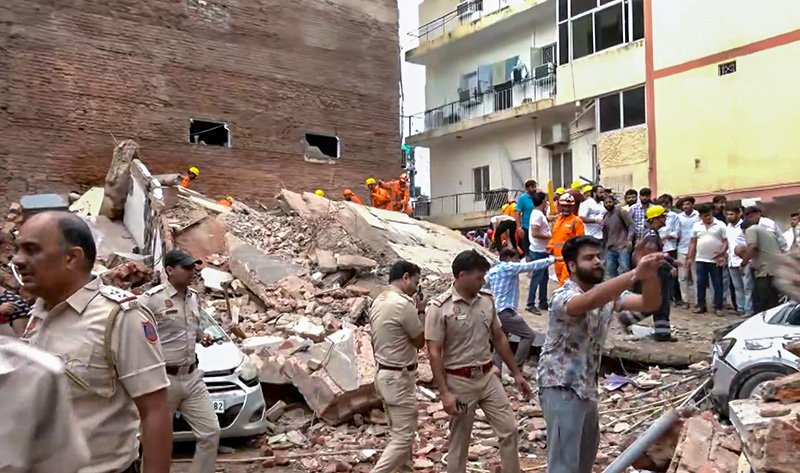 NDRF personnel conducting manual debris clearance at the Satya Niketan building collapse site in South Delhi after basement waterlogging weakened the structure.